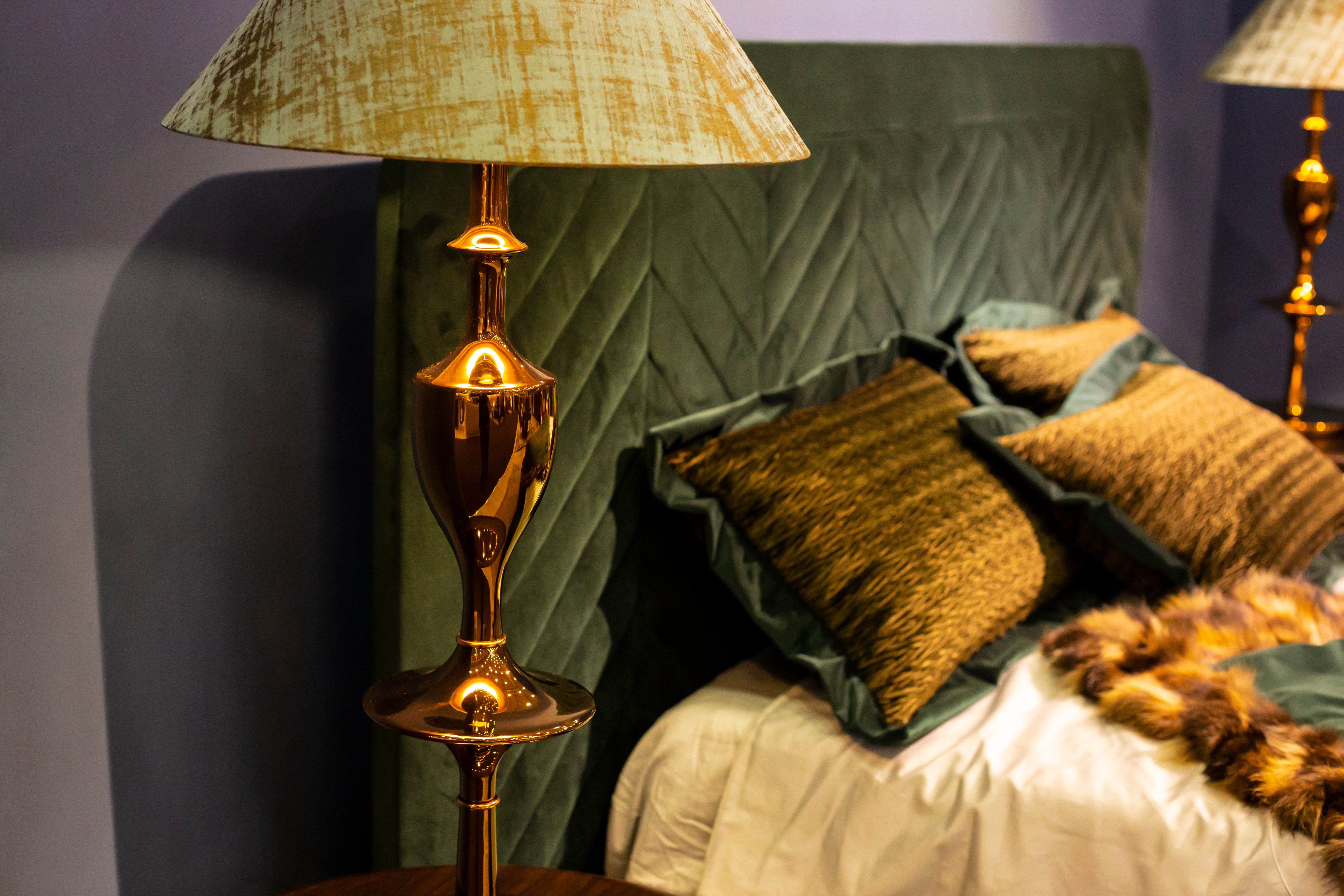  bedroom with golden floor lamp and dark green velvet headboard and expensive linens