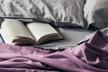 close up of bedsheets with open book under pillow